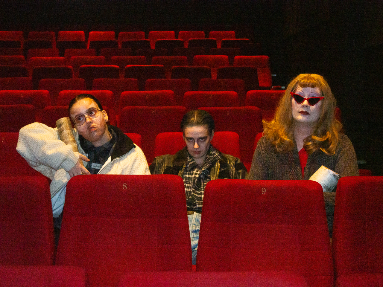 Kolme esiintyjää, jotka ovat pukeutuneet Twin Peaks -teemaiseen dragiin, istuvat tyhjässä elokuvateatterissa